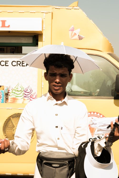 Free A street vendor in Saudi Arabia selling items in front of an ice cream truck, wearing a unique umbrella hat. Stock Photo