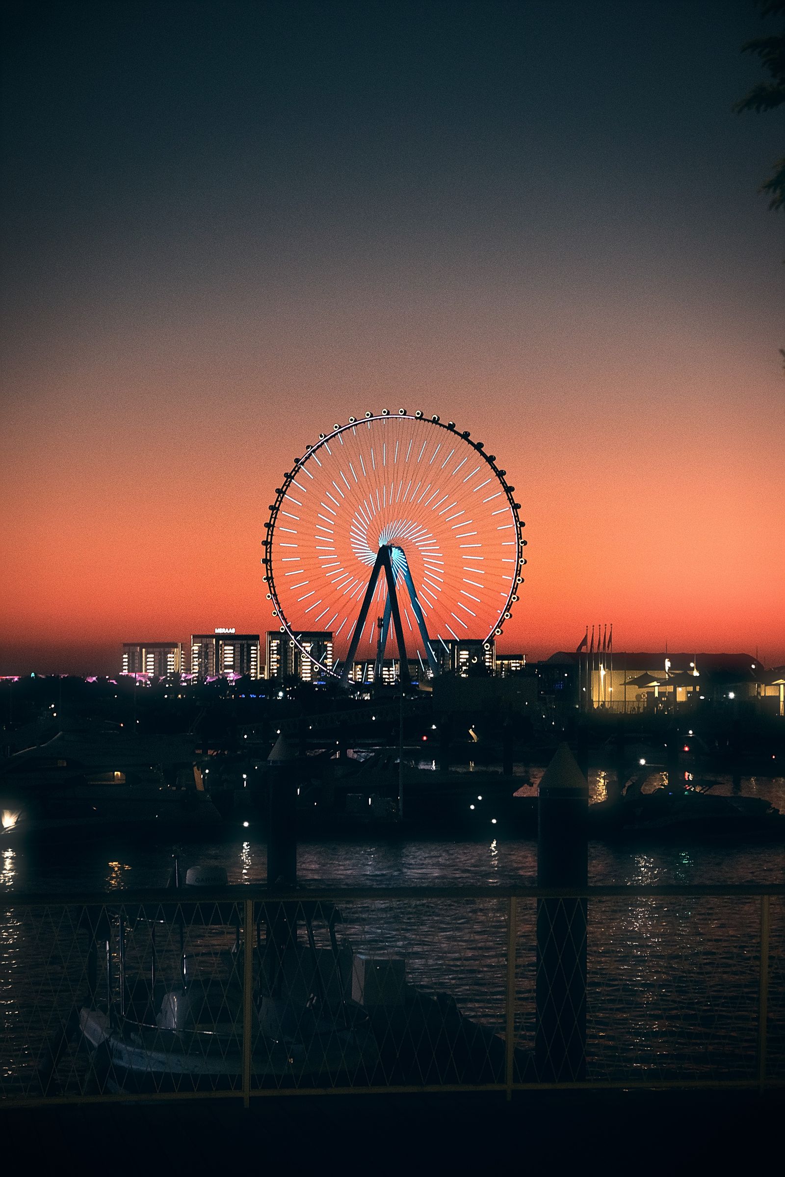 Ain Dubai wheel lit up at twilight against an orange sky, seen across the water