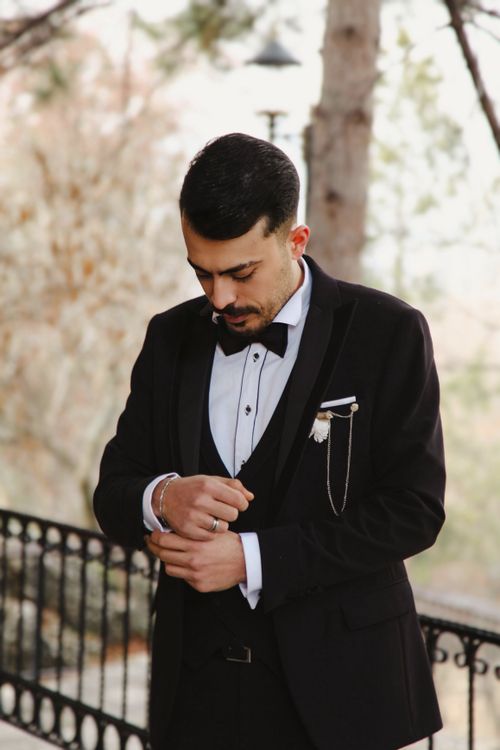 Free A groom in a tuxedo adjusts his cufflinks on a serene outdoor balcony. Stock Photo