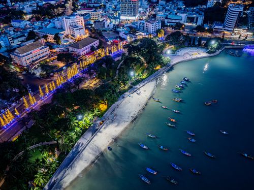 Free A stunning nighttime aerial view of a coastal city illuminated with colorful lights and boats lining the shore. Stock Photo
