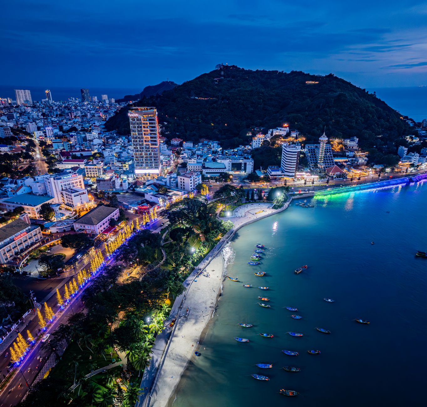 A breathtaking aerial view of a coastal city with vibrant lights at dusk.