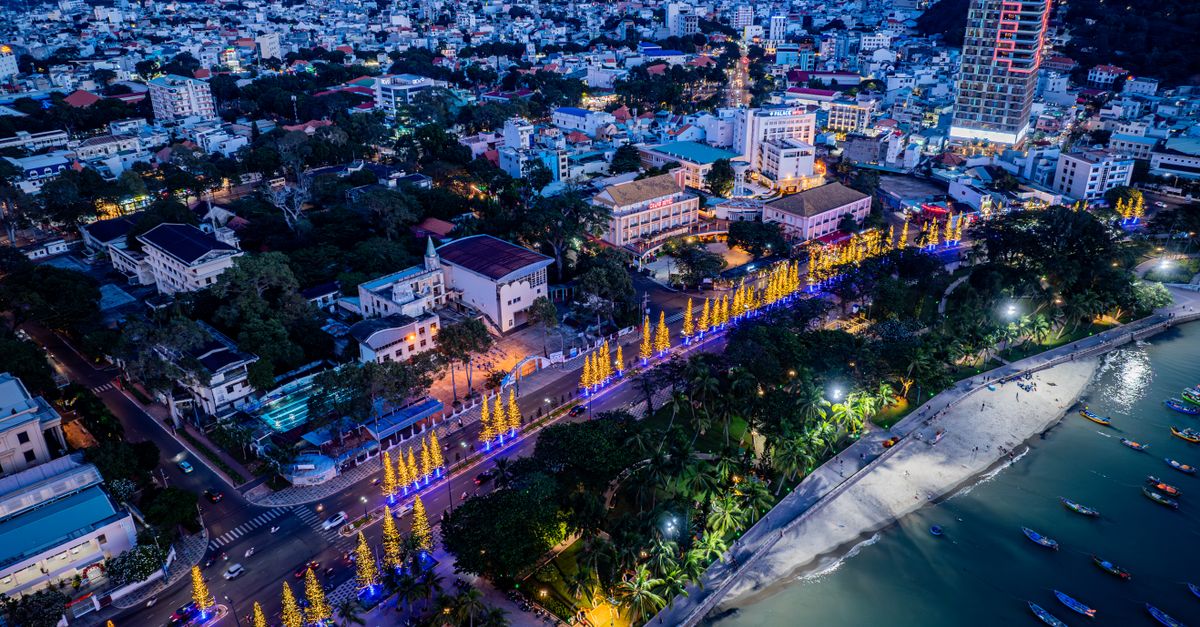 A high-angle, vibrant night view of a cityscape with beachfront and illuminated street decorations.