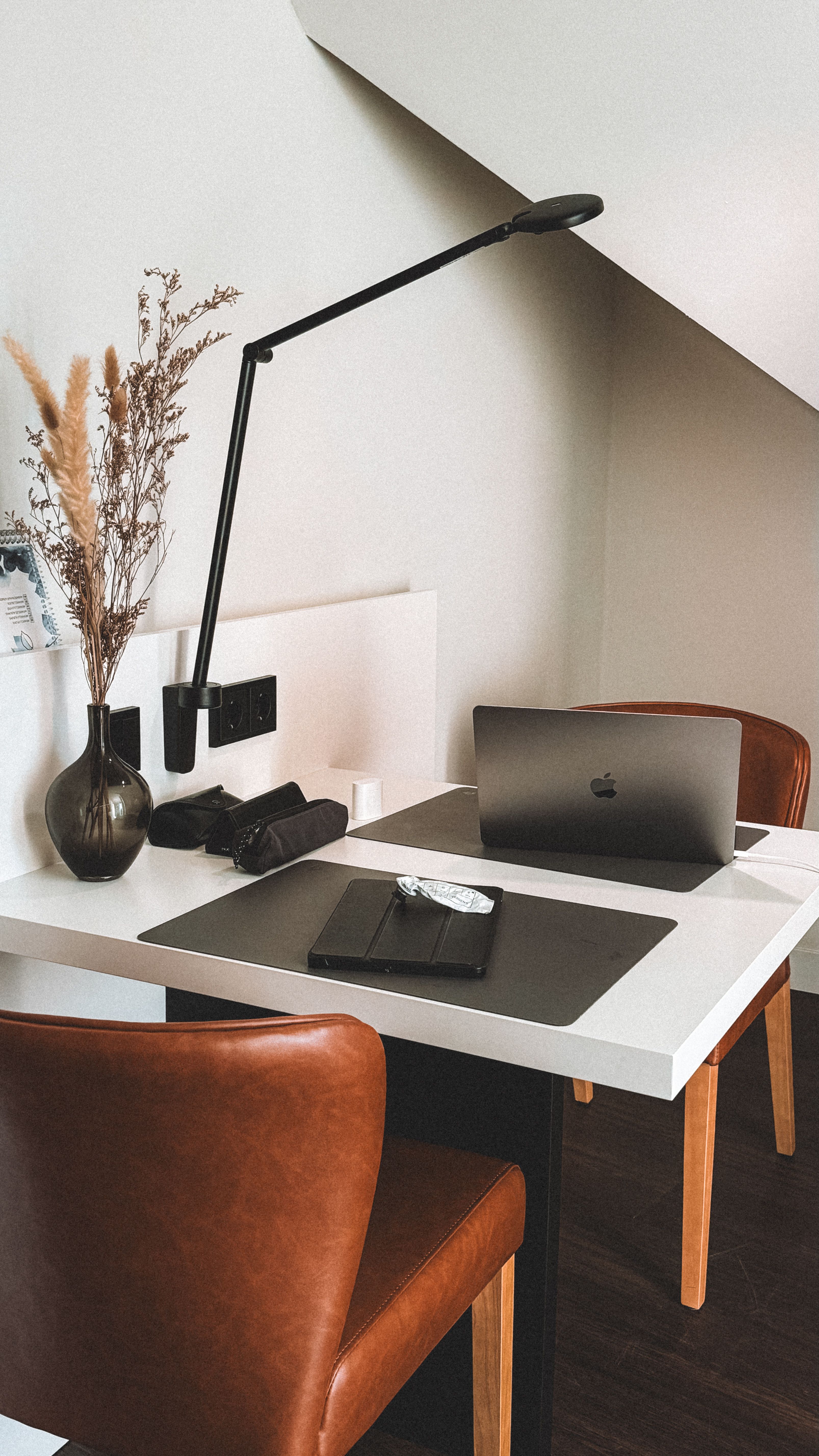 Sleek home office interior with a laptop and modern lamp on a white desk.