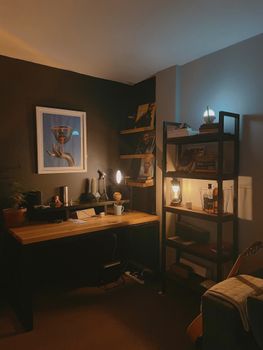 Warmly lit home office with bookshelves and modern art piece on wall.