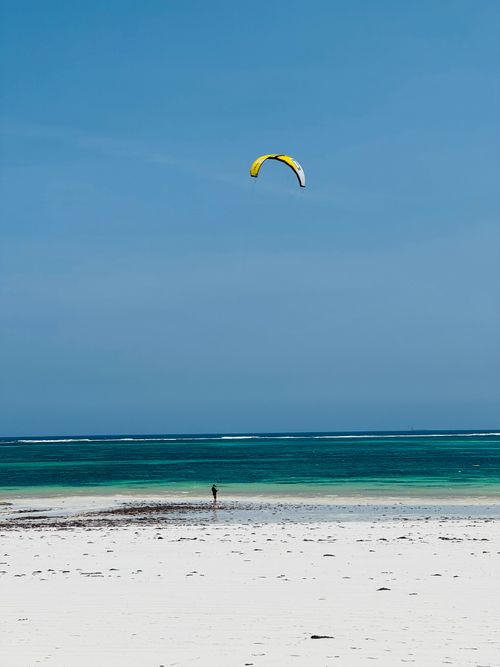 Free A lone kite surfer on a vast beach under a clear blue sky, perfect for stock photography. Stock Photo