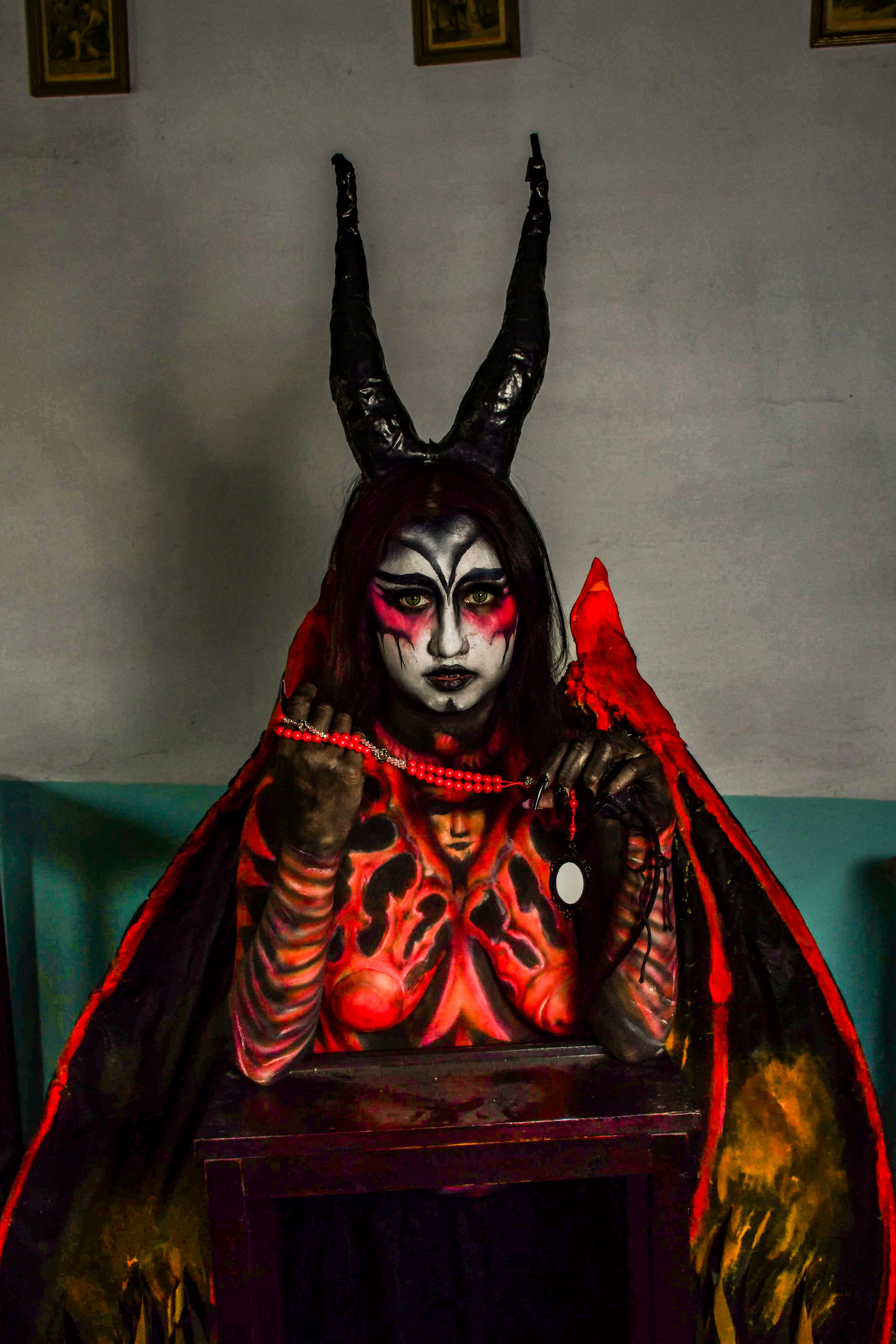 A person in a fiery demon costume with striking makeup and horns, posing indoors.
