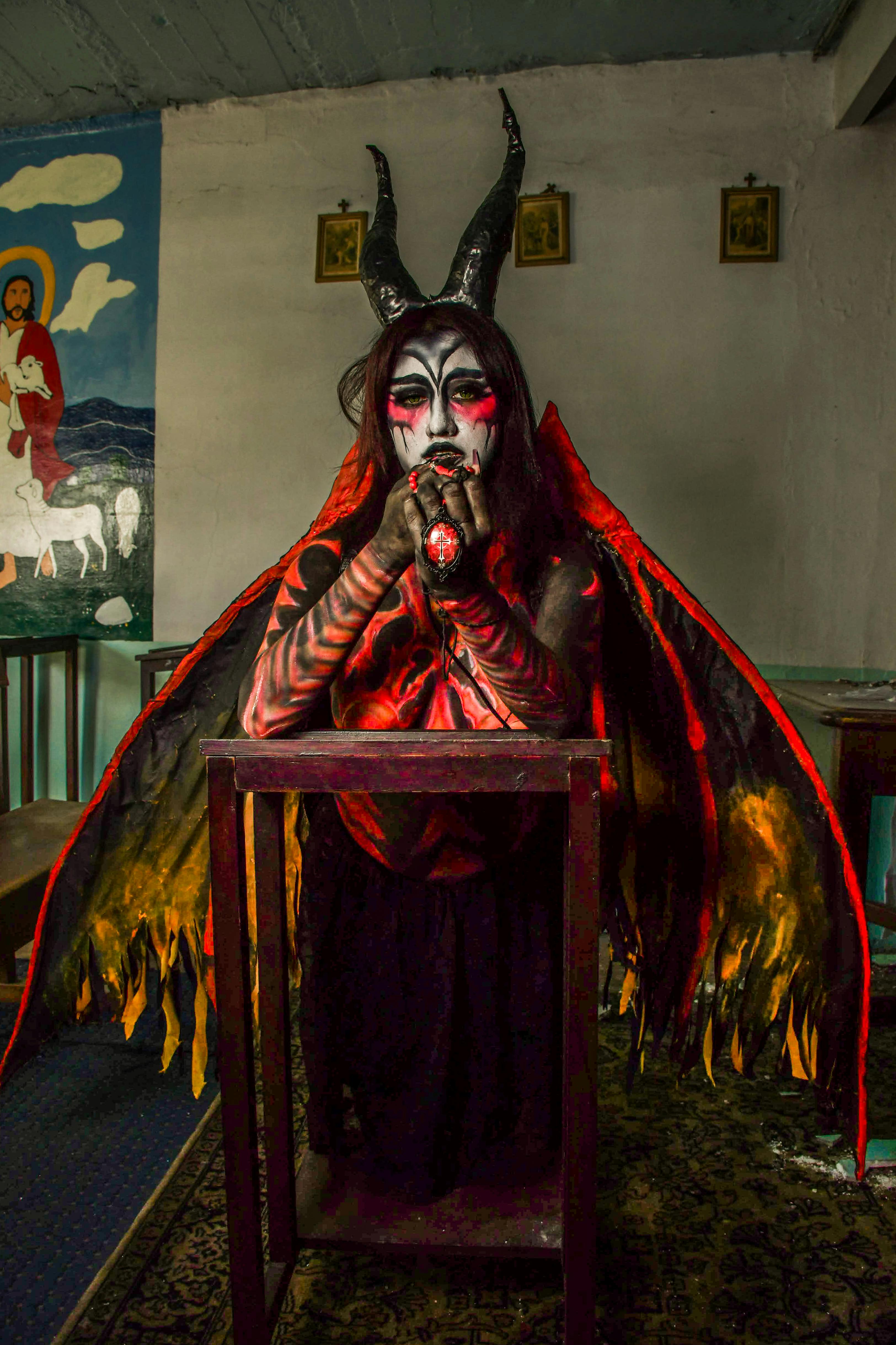grátis Uma pessoa fantasiada de diabo com rosto pintado em pé em uma sala mal iluminada. Foto profissional