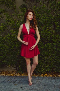 A stylish woman poses confidently in a vibrant red dress against a lush green background.