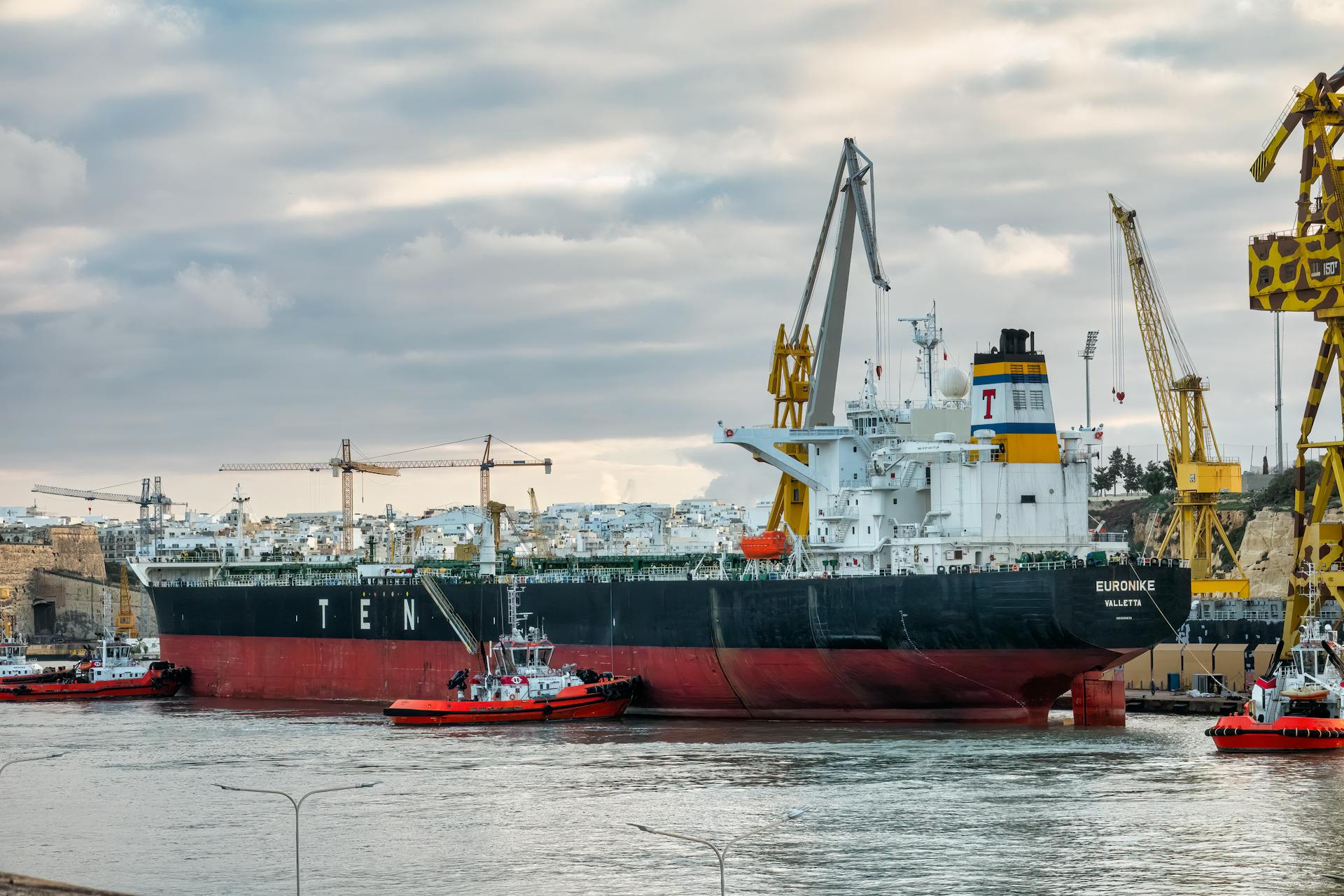 Cargo ship Euronike docked in Malta with tugboats and cranes nearby.