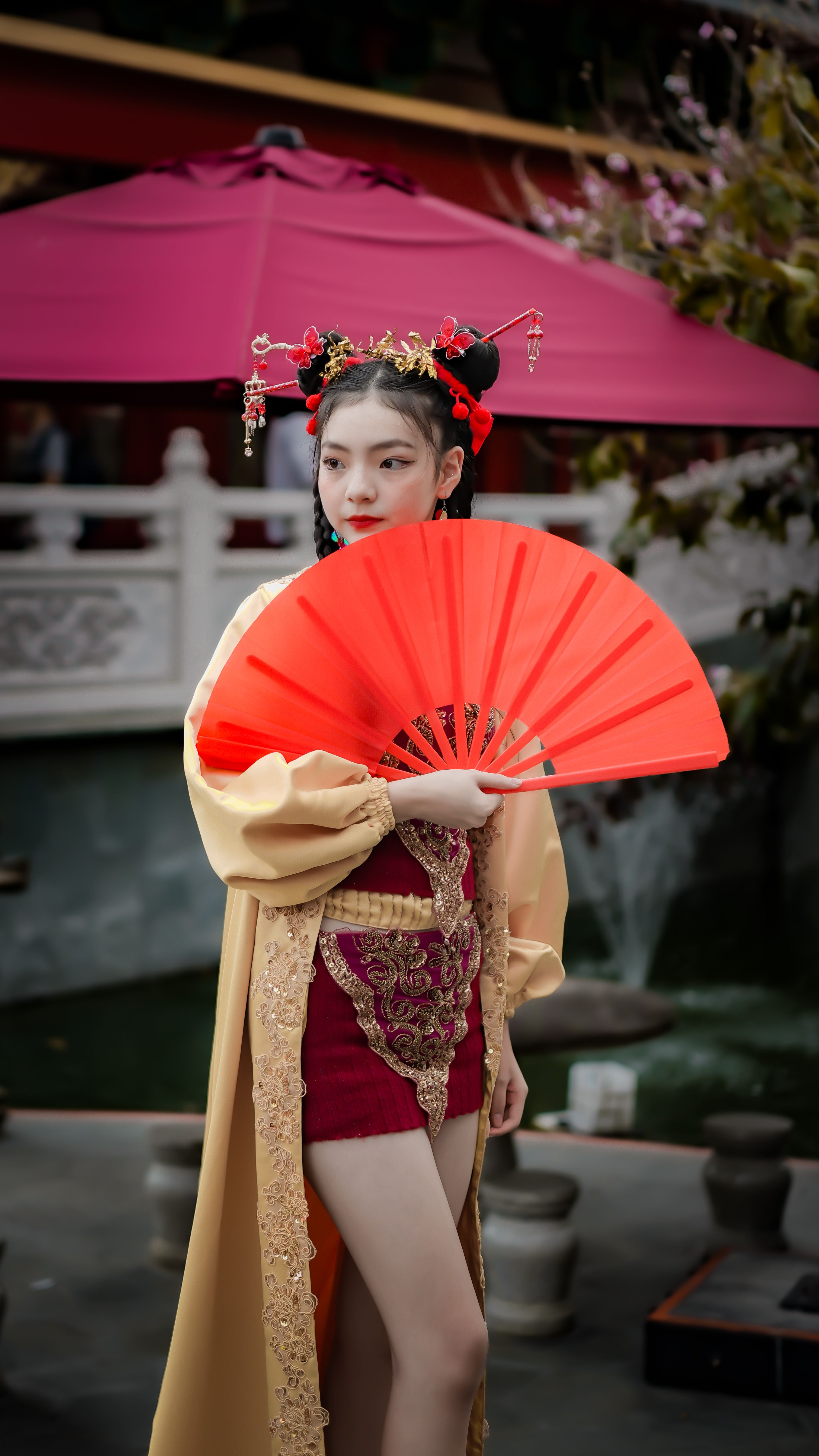 Woman in traditional Asian dress holding a red fan, embodying cultural elegance.