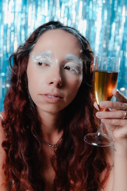 Free Woman with white eyebrows holding a champagne glass against festive backdrop. Stock Photo