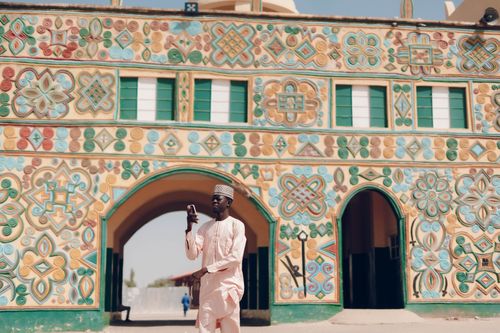 Free Man using smartphone in front of vibrant Emir's Palace architecture, Kano, Nigeria. Stock Photo