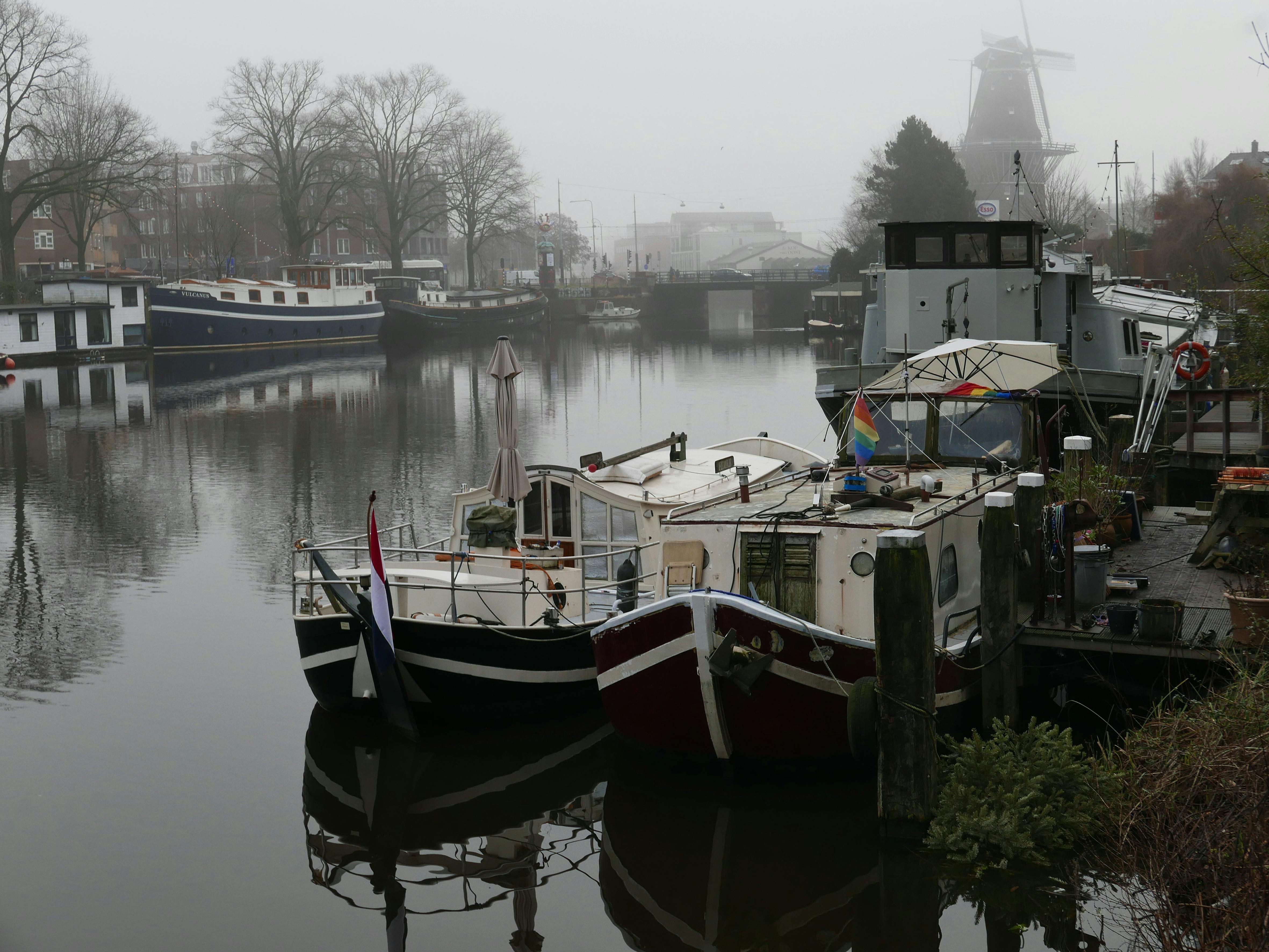 Boats and houseboats floating in the canal water under a foogy winter sky in Amsterdam city - street photography in The Netherlands by Fons Heijnsbroek, in free images.