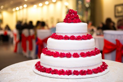 Free A stunning three-tier wedding cake adorned with vibrant red roses at a formal reception. Stock Photo
