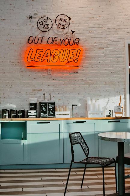 Stylish dining area featuring contemporary furniture and a vibrant neon sign saying 'Out of Your League.'