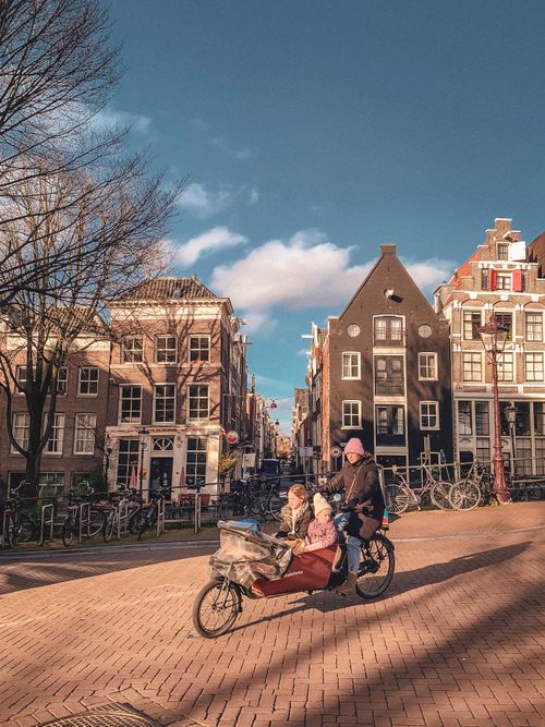 Free Warm day in Amsterdam with family cycling on historic streets, capturing the local lifestyle and architecture. Stock Photo