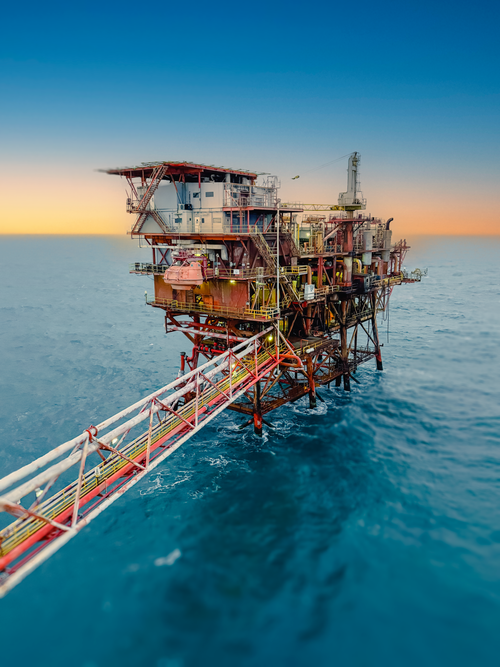 Free Aerial view of an offshore oil rig surrounded by the ocean at sunset, under a clear sky. Stock Photo