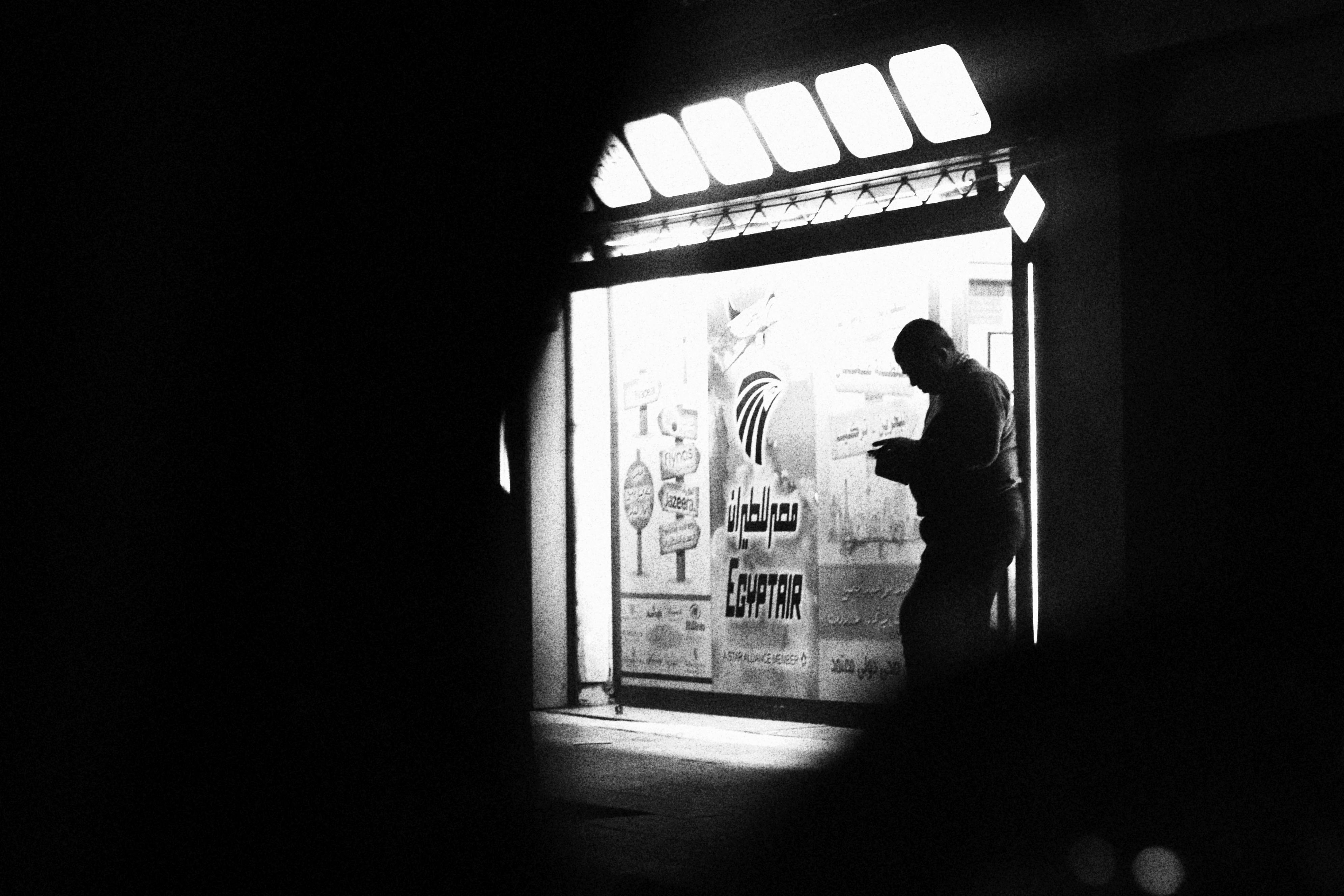 grátis Uma silhueta contemplativa capturada em frente a uma placa da EgyptAir, em uma cena de rua em preto e branco. Foto profissional