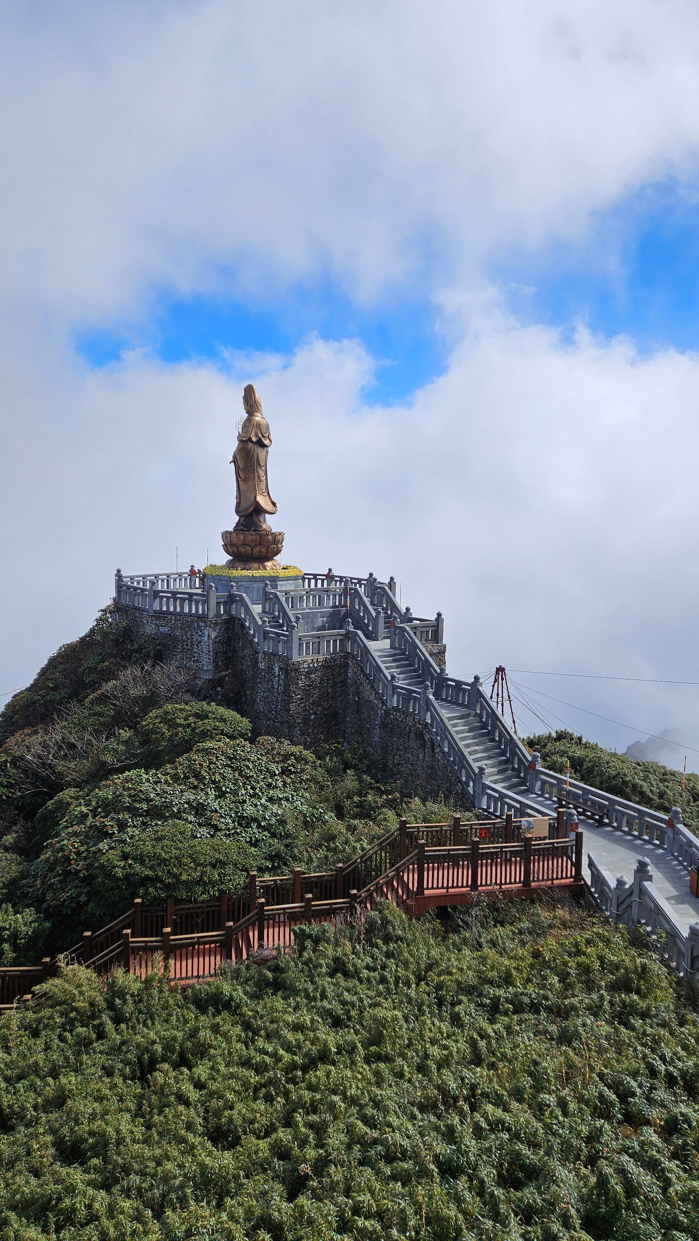 Majestic statue on Mount Fansipan's peak surrounded by lush greenery and blue sky.