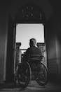 黑白照片中，一名坐在轮椅上的男子透过敞开的门向外望去，画面透着孤独