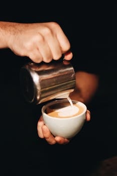 Captivating close-up of barista skillfully pouring latte art into a cup of coffee with creamy milk.