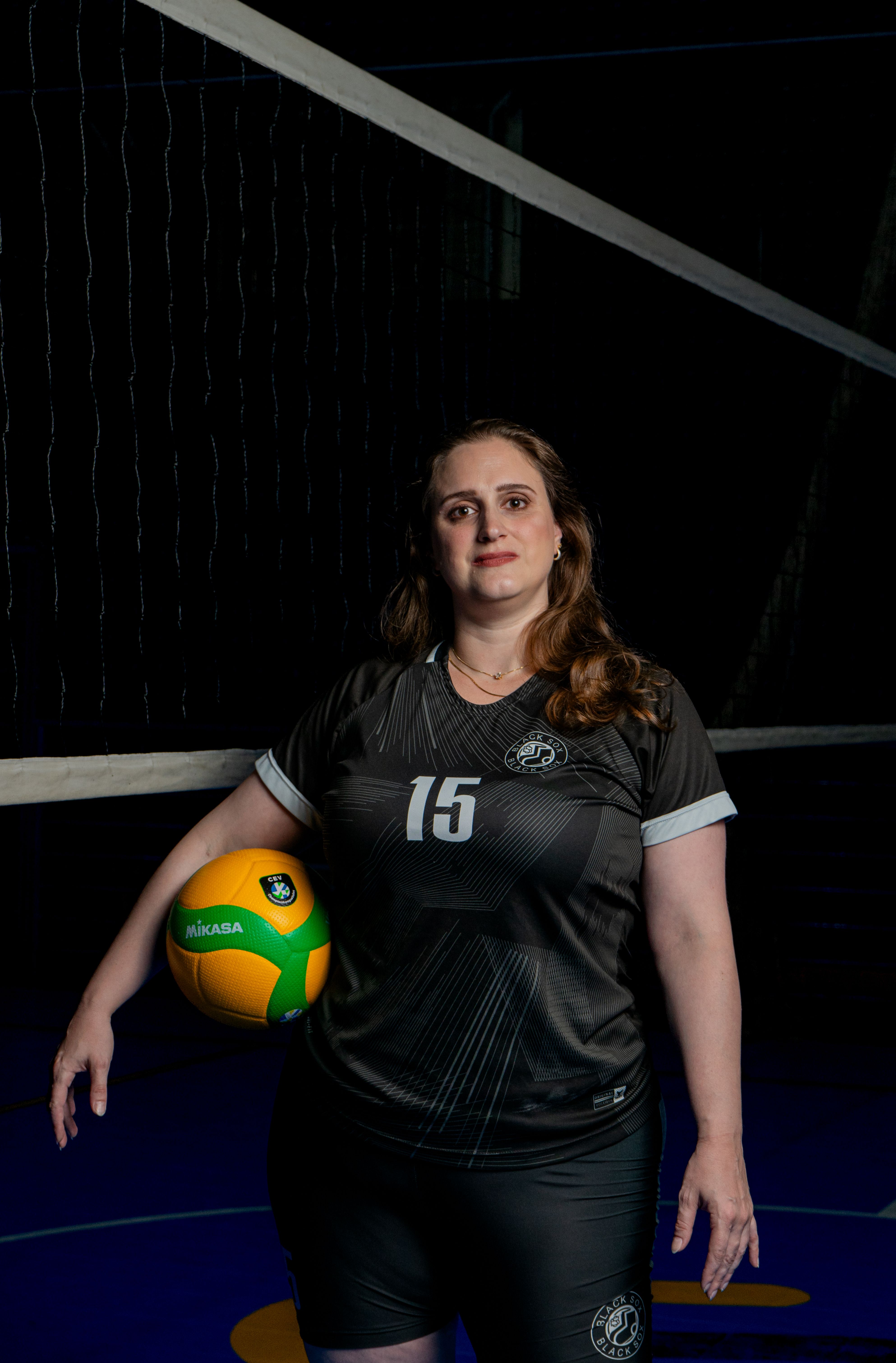 Focused female volleyball player in sports uniform holding a ball on an indoor court.