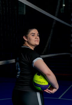 A female volleyball player poses with a ball on an indoor court, ready for a match.