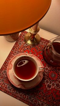 Warm tea in a decorative cup under a soft lamp light, creating a cozy ambiance.