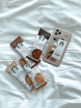 Flat lay of four coffee packs and phone on a white sheet, perfect for coffee lovers.
