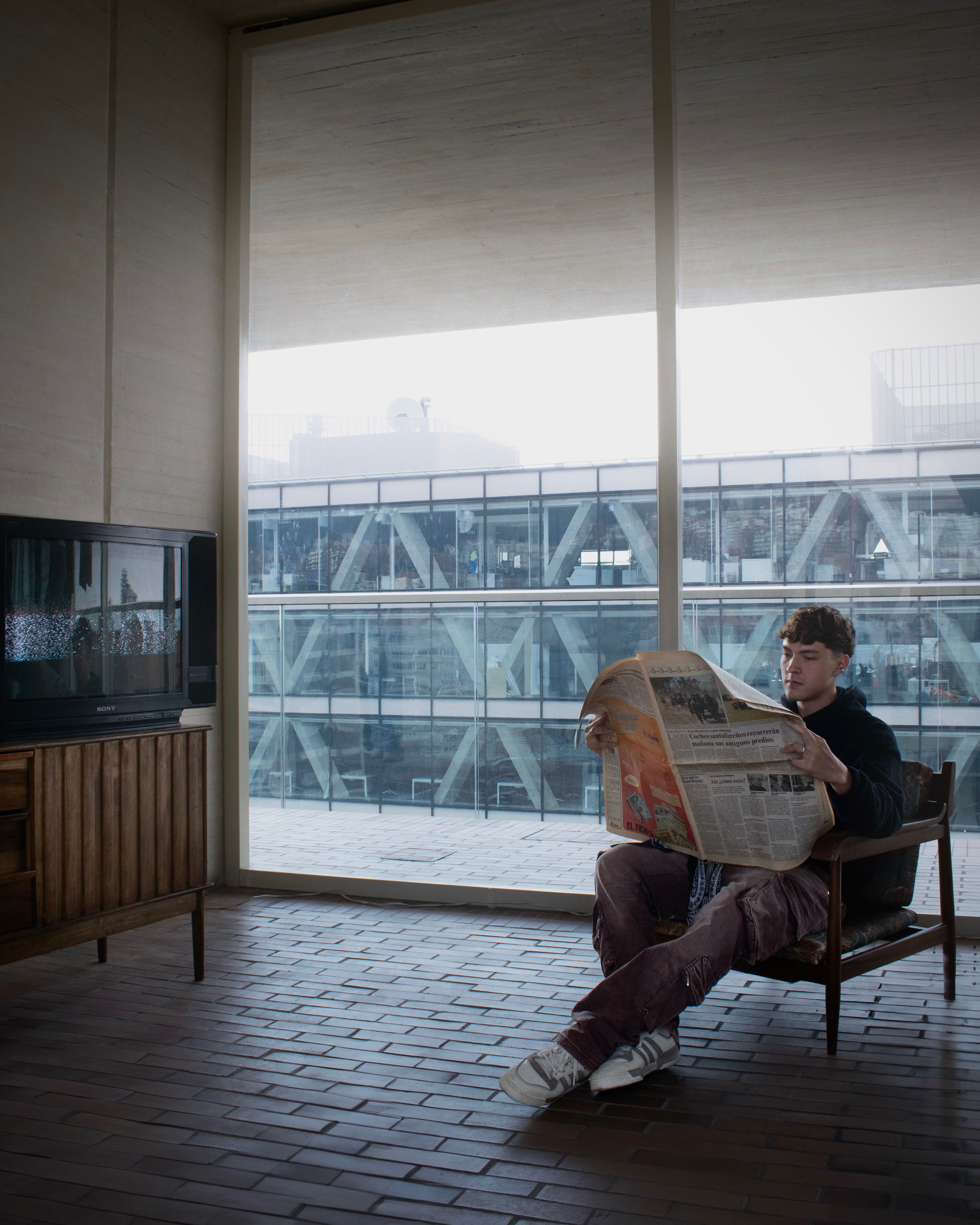 A man reading a newspaper in an empty office space with brick flooring