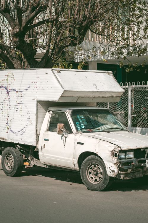 Free Aged white pickup truck parked on a sunny city street, showing signs of wear. Stock Photo