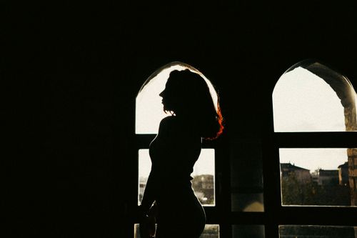 Free Artistic silhouette of a woman standing by an arched window, creating a dramatic shadow effect. Stock Photo