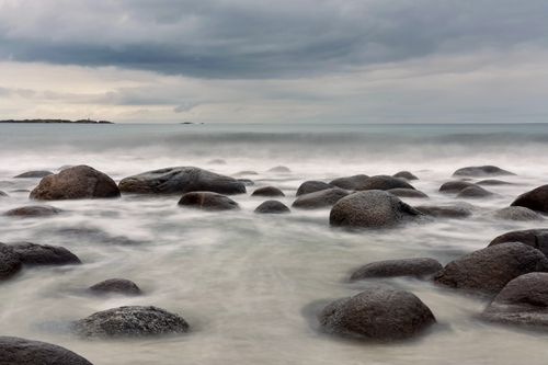 Free Tranquil seascape featuring smooth rocks and gentle ocean waves under a cloudy sky. Stock Photo