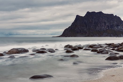 Scenic rocky beach with mountain and calm sea under cloudy sky.