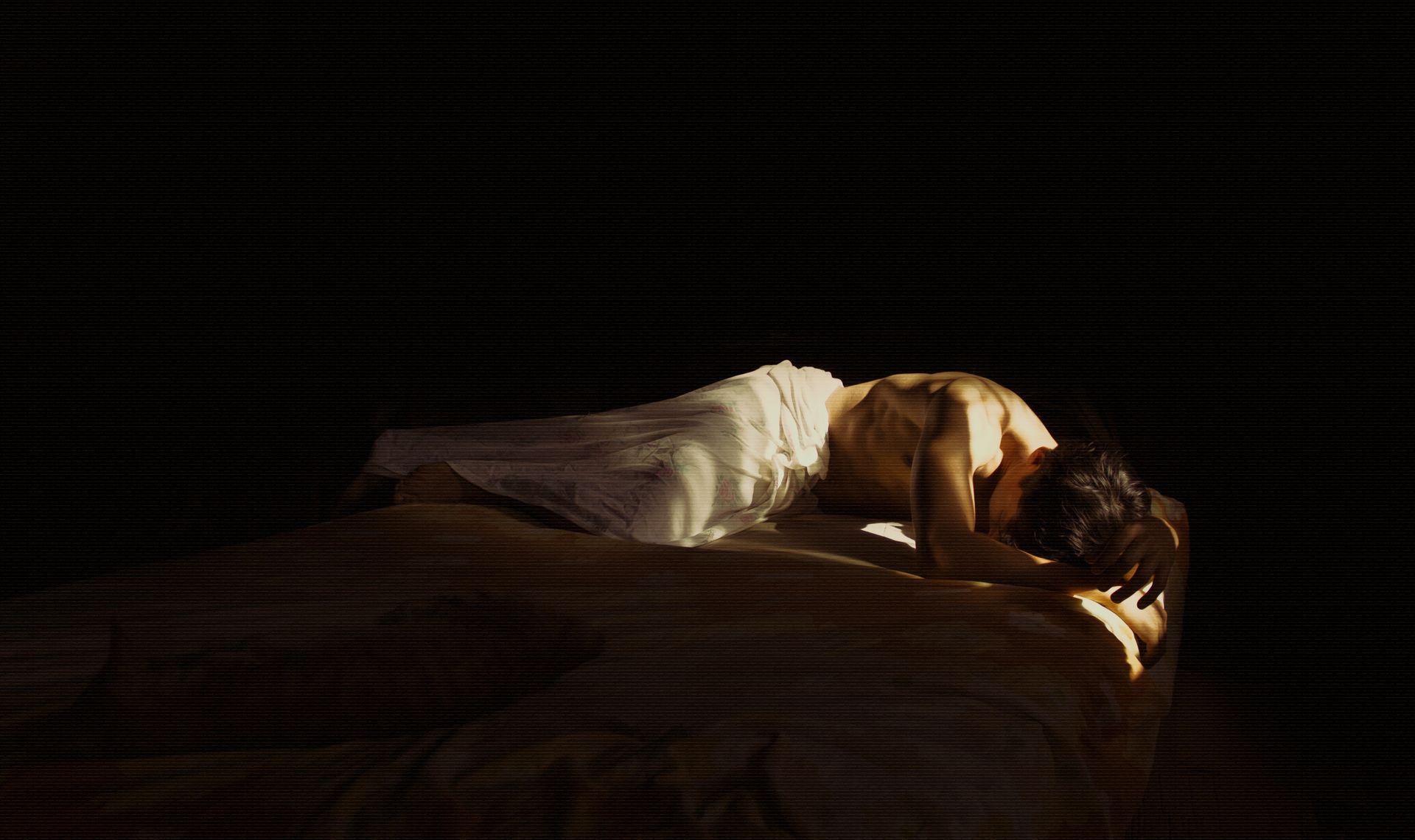 Artistic portrait of a man resting on a bed in dramatic low lighting.