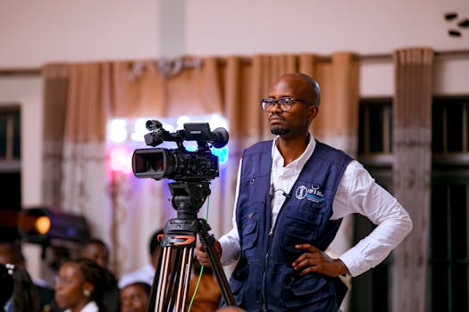A focused cameraman operates a video camera indoors, capturing an event.