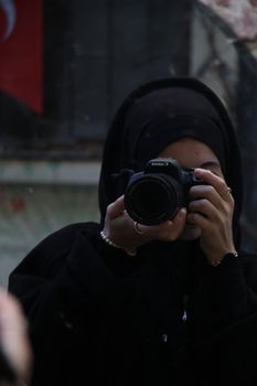 A woman in a hijab takes a photo with a camera in an urban setting, showcasing cultural diversity.