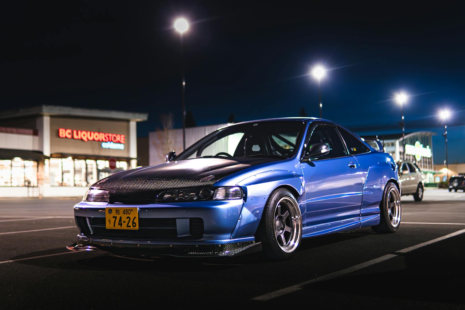 Blue sports car with custom modifications in a night parking lot setting.