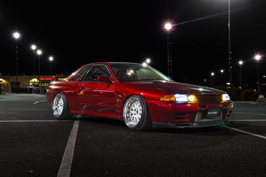 Red sports car showcased in well-lit empty parking lot at night.