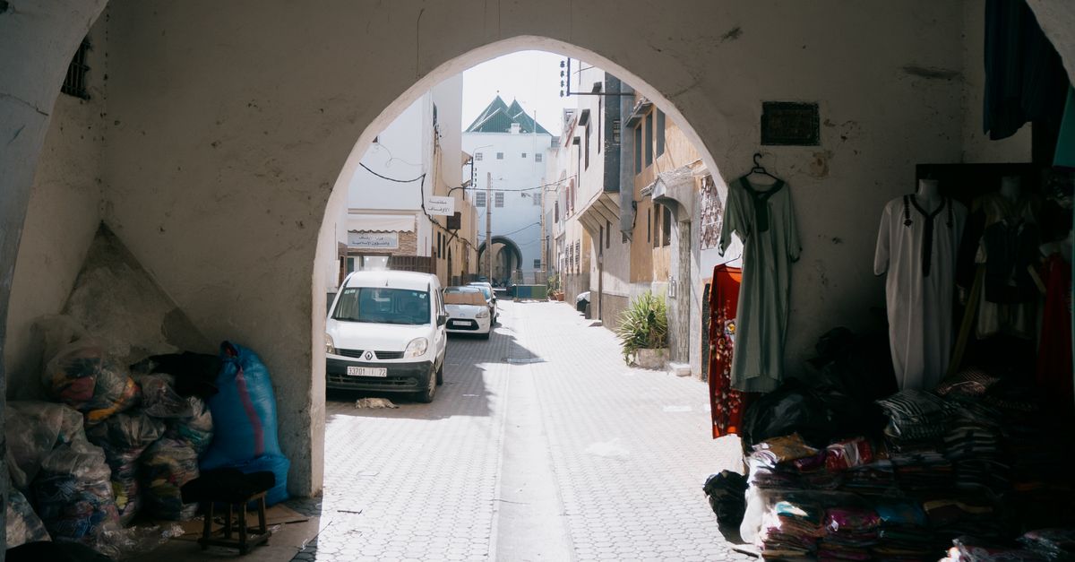 Scenic view of a Moroccan street through an archway with textiles and parked cars.