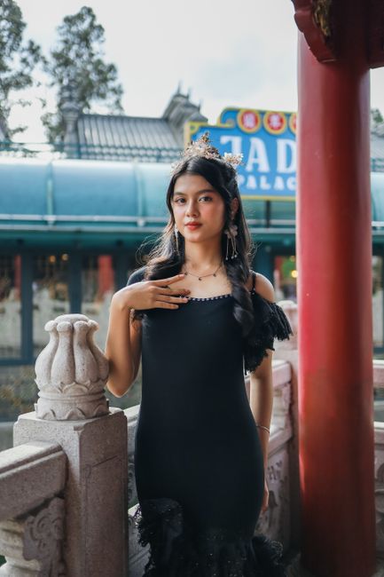 An elegant woman in black dress posed against traditional Asian architecture, showcasing cultural style.