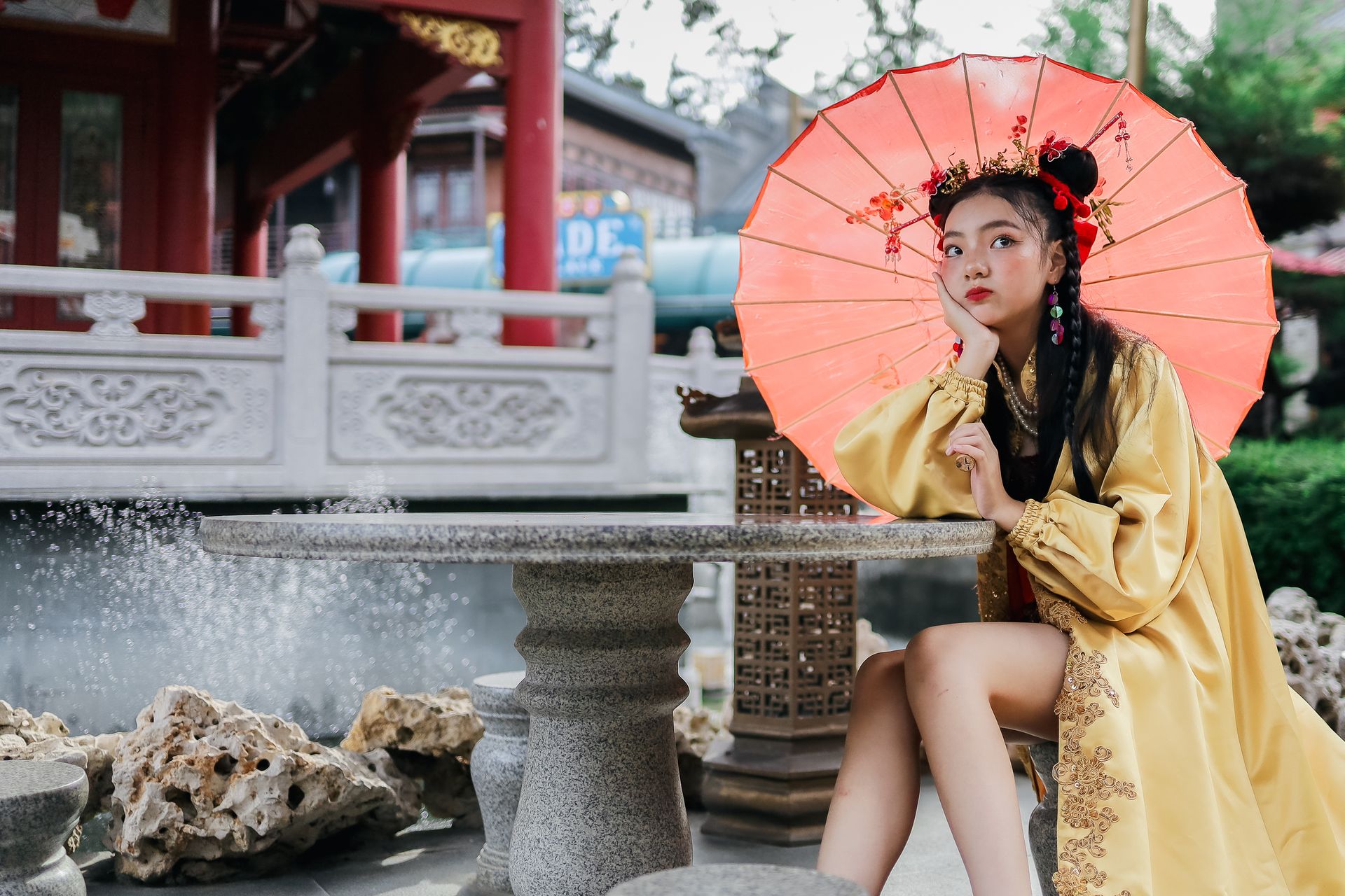 Woman wearing traditional Chinese attire sitting outdoors with a vibrant parasol.