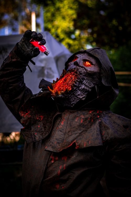 Free A dark, hooded figure with glowing eyes raising a vial in an eerie outdoor setting. Stock Photo
