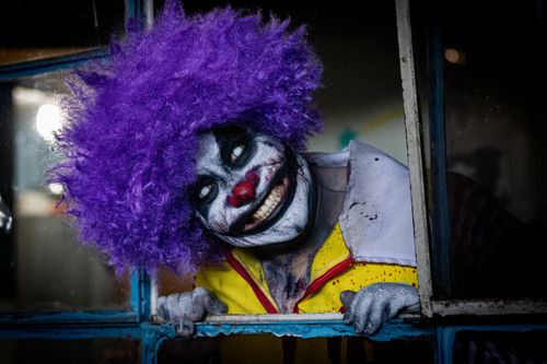 Free Terrifying clown with purple wig and makeup peering through a window at night. Stock Photo