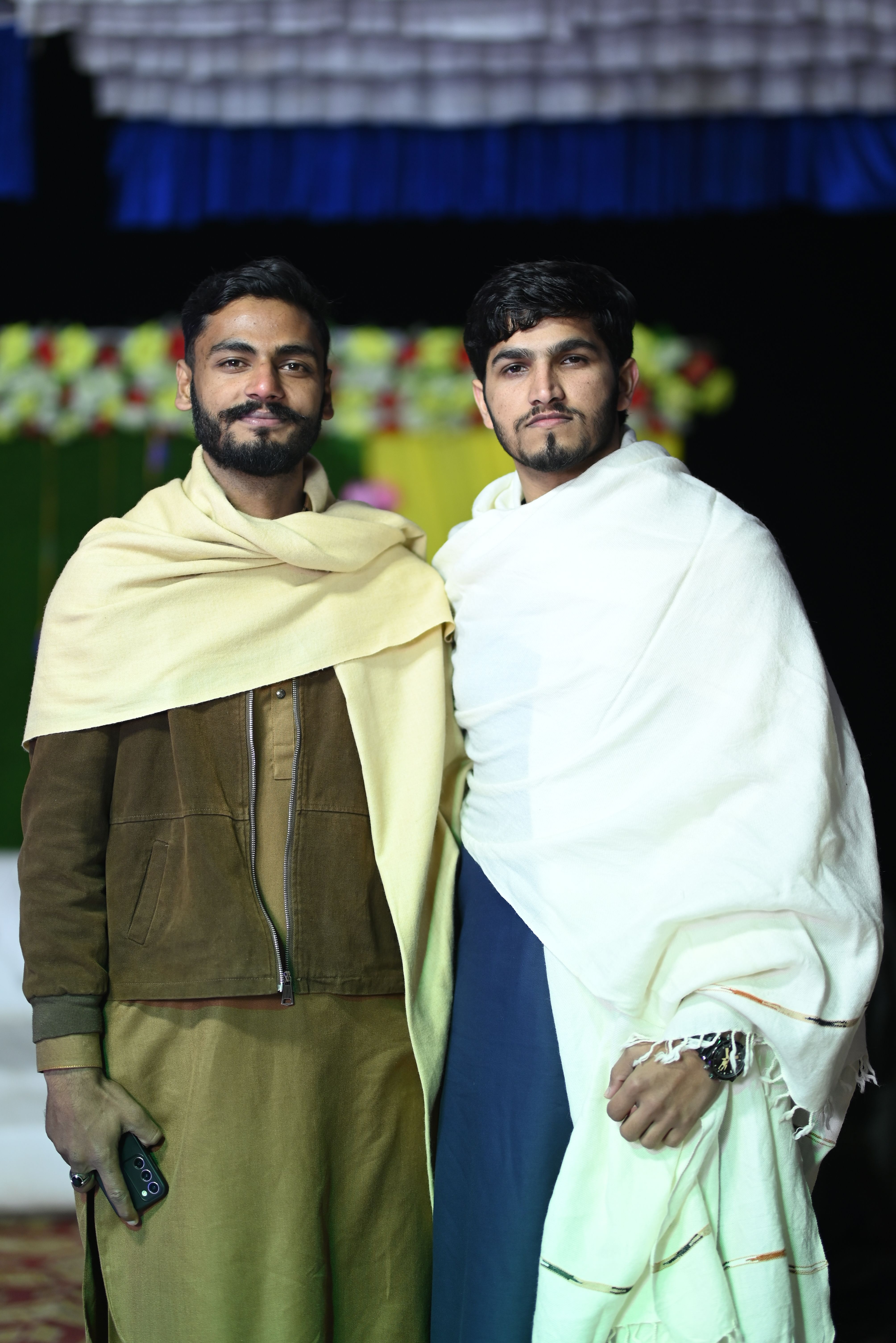 Two brothers in elegant shawls at a traditional South Asian event.