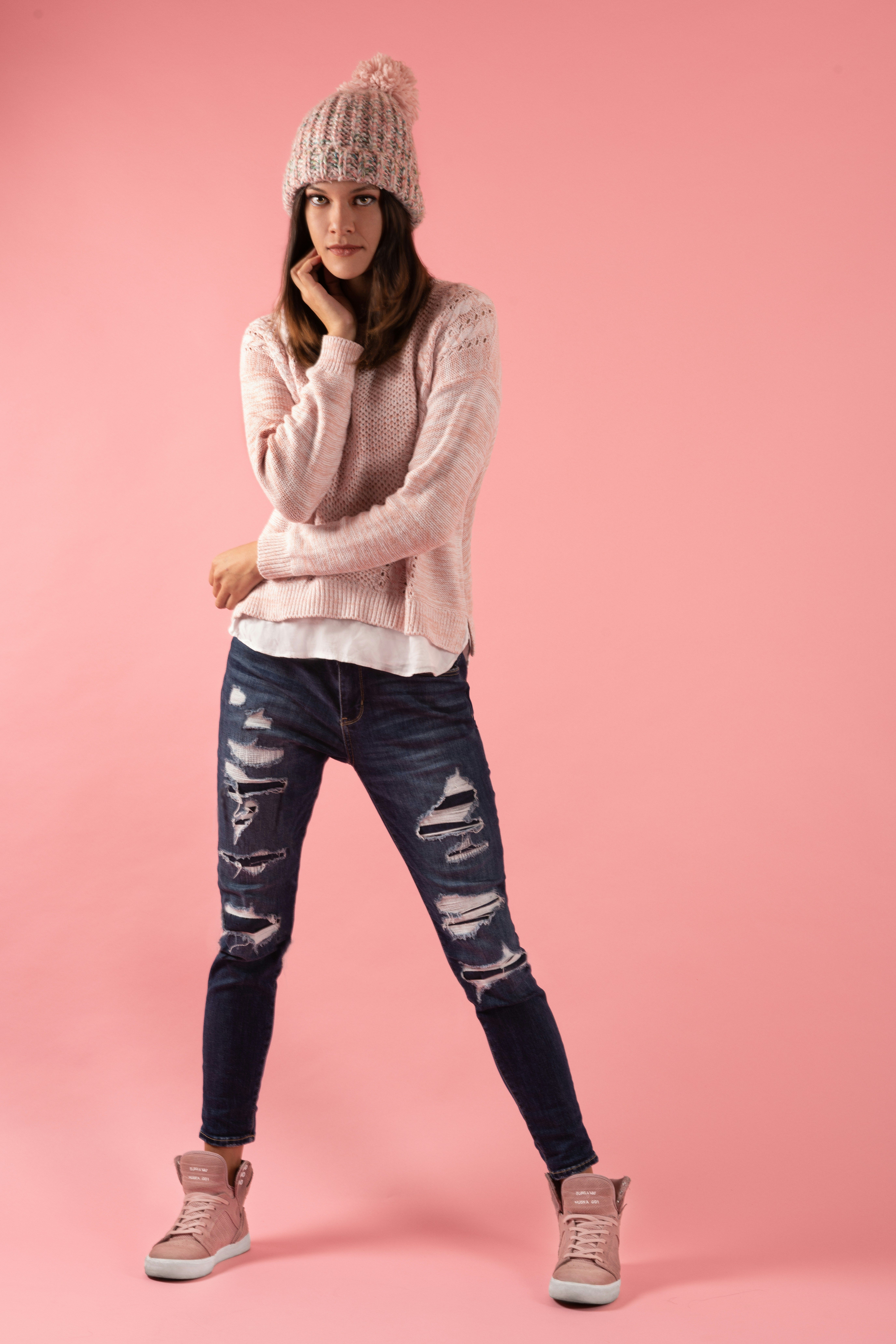 Stylish young woman in knitwear and denim poses against a pink backdrop.