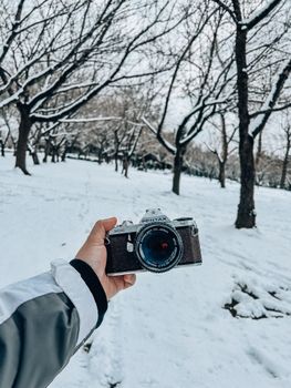 Hand holding a vintage camera in snowy Central Park, New York.