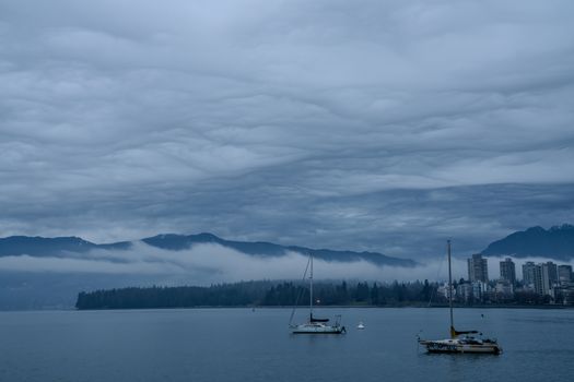 Sailboats on moody waterfront in Vancouver, Canada with misty mountains and skyline.