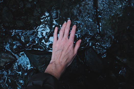 一只手在自然、平静的户外环境中伸出，触摸水面