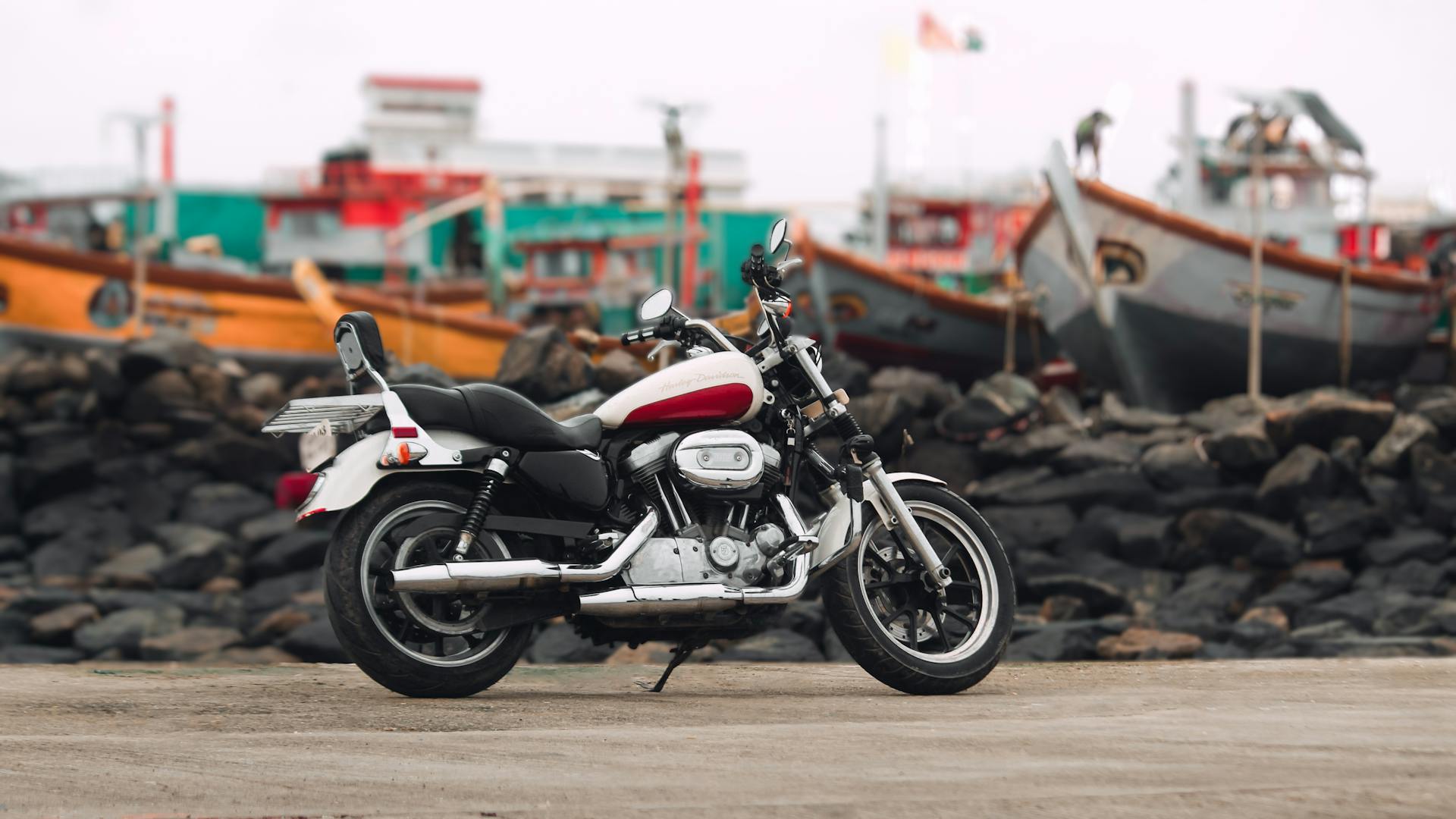 A Harley Davidson motorcycle parked by fishing boats in Mumbai harbor, capturing urban lifestyle and adventure.